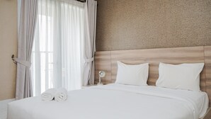 Cama bem arrumada com lençóis e almofadas brancos, mesa de cabeceira com abajur e cortinas finas na janela.