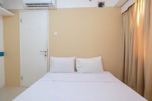 A hotel room with a bed, white curtains, a door, and an air conditioning unit.