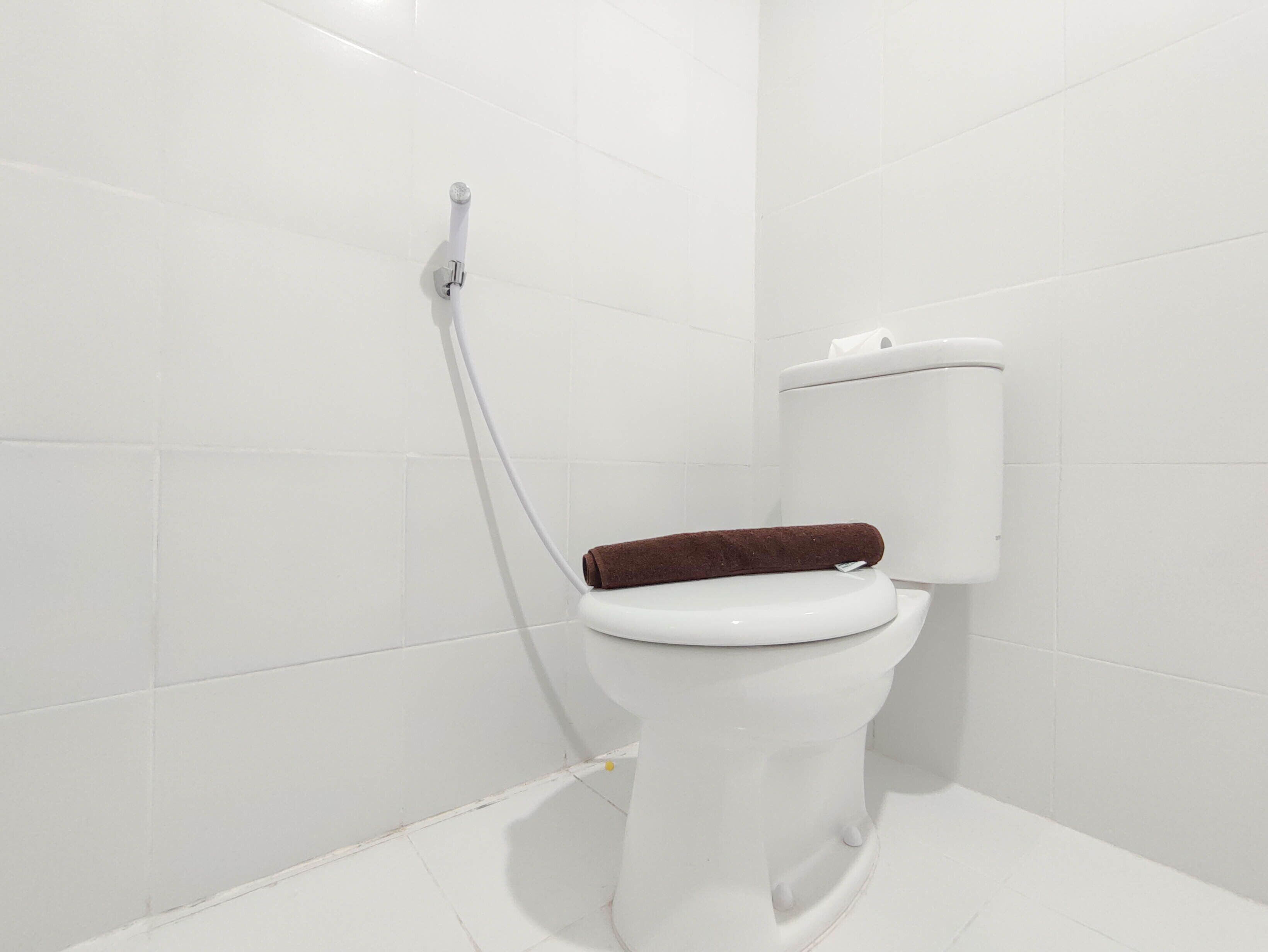 A white toilet with a brown seat in a bathroom with white tiled walls.