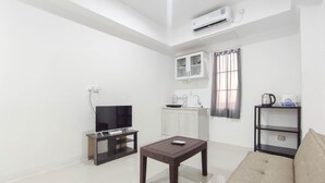 A modern living room with a flat-screen TV, a coffee table, a sofa, a kitchen area with a sink, and an air conditioning unit. - Good Deal 1Br At Paltrow City Apartment (Semarang)