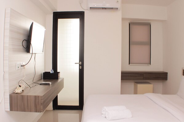 Une chambre d’hôtel avec une coiffeuse en bois, un téléviseur à écran plat fixé au mur, un lit recouvert d’une couette blanche et une fenêtre donnant sur un paysage agréable.