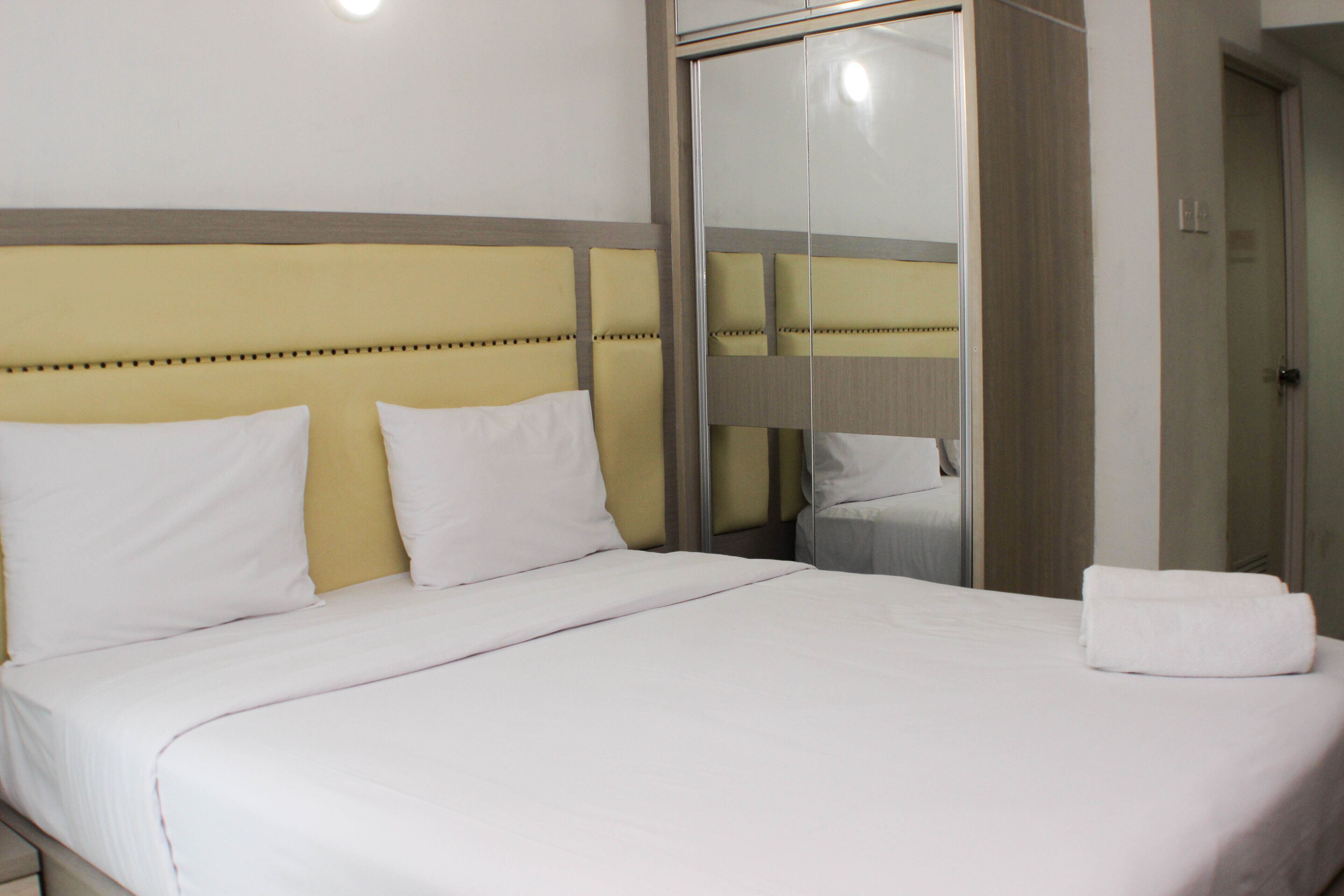 A neatly made bed with white linens, a headboard with a yellow panel, and a mirror cabinet with a sliding door.