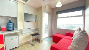Ein kompakter Wohnbereich mit Küchenzeile, einem an der Wand befestigten Flachbildfernseher, einem roten Sofa und einem großen Fenster mit Blick auf die Stadt.
