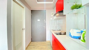 Eine moderne Küche mit roter Arbeitsplatte, Spüle und Herd. Eine Tür führt in einen anderen Raum, und in der Ecke steht ein kleiner Hocker.