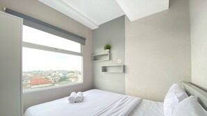 Ein modernes Hotelzimmer mit großem Fenster, einem ordentlich bezogenen Bett und eingebauten Regalen mit einer kleinen Pflanze.