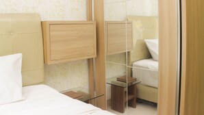A hotel room with a bed, a bedside table, a mirror, and a small wooden cabinet. - Warm And Homey 2Br At Springlake Summarecon Bekasi Apartment (Bekasi)
