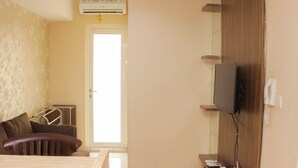 A hotel room with a bed, a desk, a television, and a door leading to the outside. - Warm And Homey 2Br At Springlake Summarecon Bekasi Apartment (Bekasi)