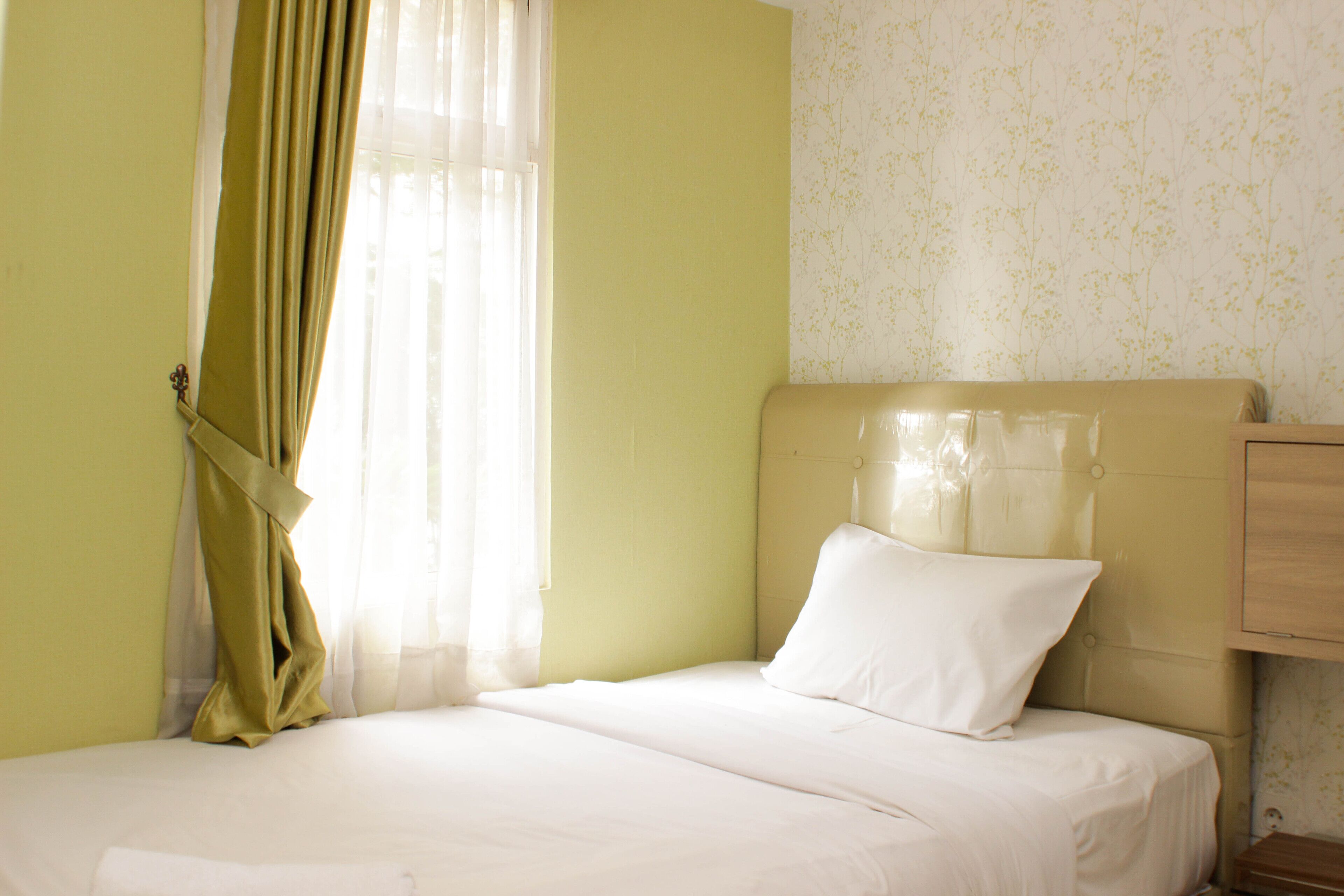 A hotel room with a bed, a nightstand, and a window with curtains.