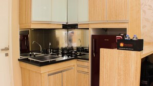 A compact kitchen with wooden cabinets, a black countertop, a stainless steel sink, a gas stove, and a refrigerator. - Warm And Homey 2Br At Springlake Summarecon Bekasi Apartment (Bekasi)