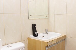 Ein Badezimmer mit weißem Waschbecken, einem Spiegel und Pflegeprodukten auf der Ablagefläche.