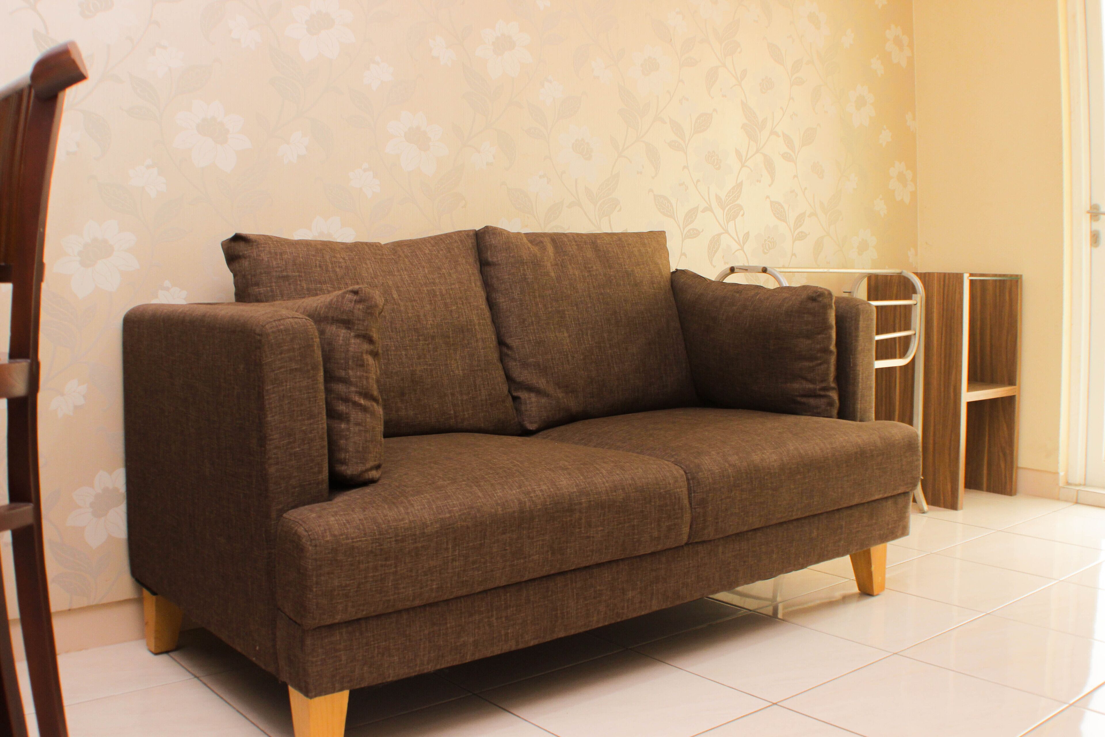 A brown sofa with cushions in a room with floral wallpaper and a tiled floor.