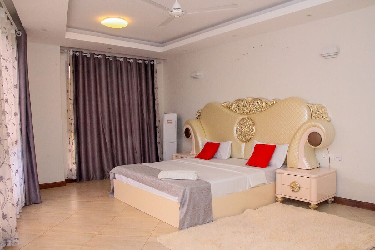 A bedroom with a large bed, a ceiling fan, and a window with curtains.
