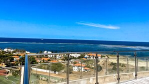 Vista sul litorale da un balcone, con cielo sereno, oceano e edifici in primo piano.
