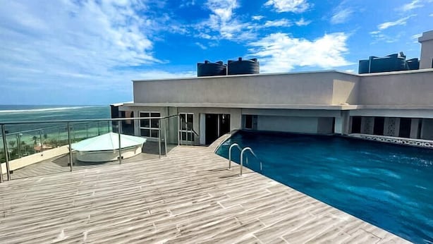 Una piscina sul tetto con un solarium in legno, cielo azzurro limpido e vista sull'oceano.