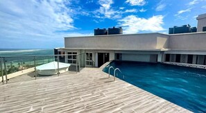 Ein Pool auf dem Dach mit Holzboden, blauem Himmel und Blick auf das Meer.