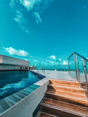 A swimming pool with a wooden deck and glass railings, overlooking a clear blue sea. - Stay.Plus Antalya Luxury Apartment (Mombasa)