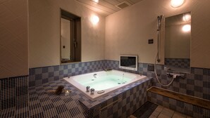 A modern bathroom with a freestanding bathtub, a handheld showerhead, and a small screen mounted on the wall. - HOTEL ZEN RIKYU CHIBA-SHIROI (Shiroi)
