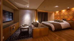A modern hotel room with a sofa, a bed, a flat-screen TV, and a wooden accent wall. - HOTEL ZEN RIKYU CHIBA-SHIROI (Shiroi)