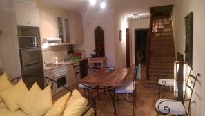 A compact kitchen with modern appliances, a dining area with metal chairs, and a staircase leading to another level.