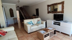 Un soggiorno con un divano, una televisione, un mobile e una scala sullo sfondo.