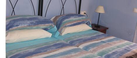 A bed with a striped bedspread and pillows, a bedside table with a lamp, and a wall-mounted power outlet.