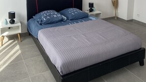 Un dormitorio moderno con una cama, una mesita de noche, un espejo montado en la pared y un elemento decorativo.