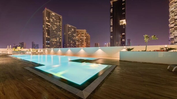 A rooftop pool with a view of high-rise buildings at night. - JVC Studio park view fully equipped - 360 vacation (Dubai)