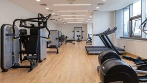 A gym with cardio machines, weightlifting equipment, and a wooden floor. - JVC Studio park view fully equipped - 360 vacation (Dubai)