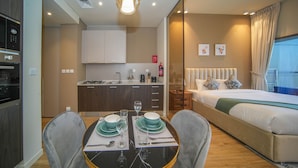 A modern hotel room with a dining area, kitchenette, and a large bed with a view. - JVC Studio park view fully equipped - 360 vacation (Dubai)