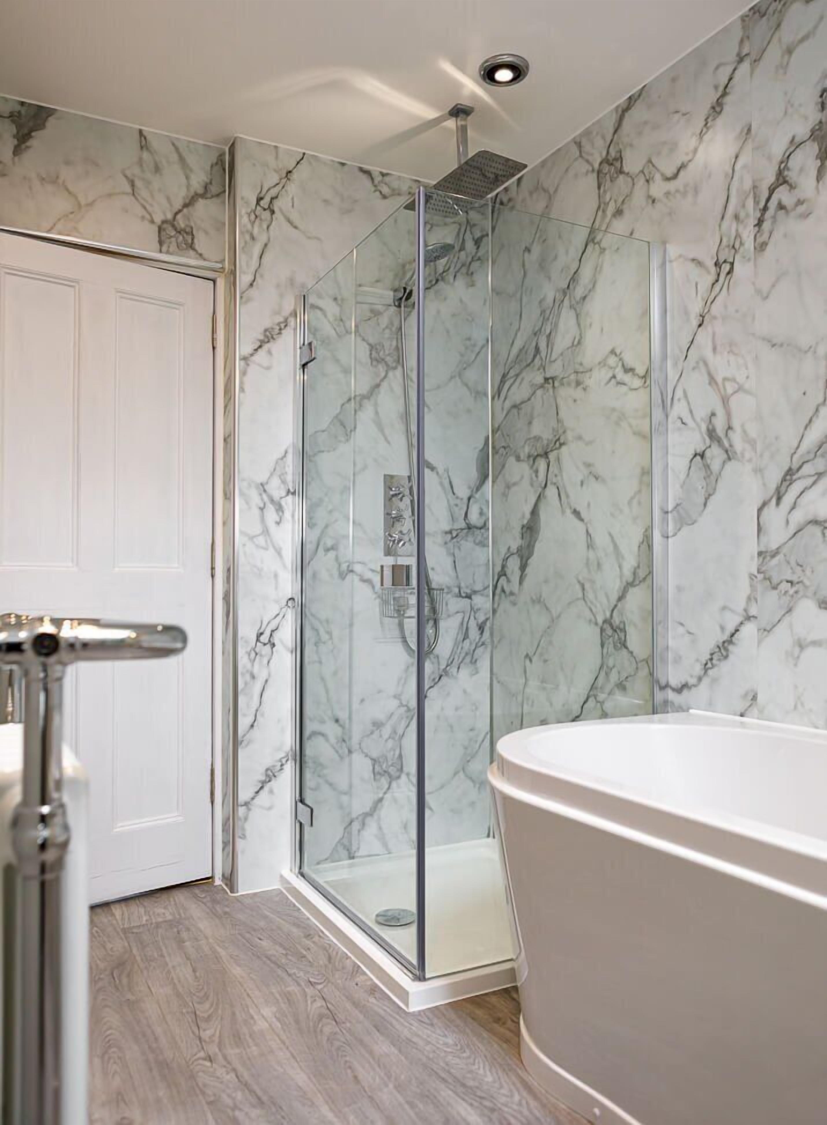 Een badkamer met een douchecabine van glas, een vrijstaand bad en wanden met een marmerlook.