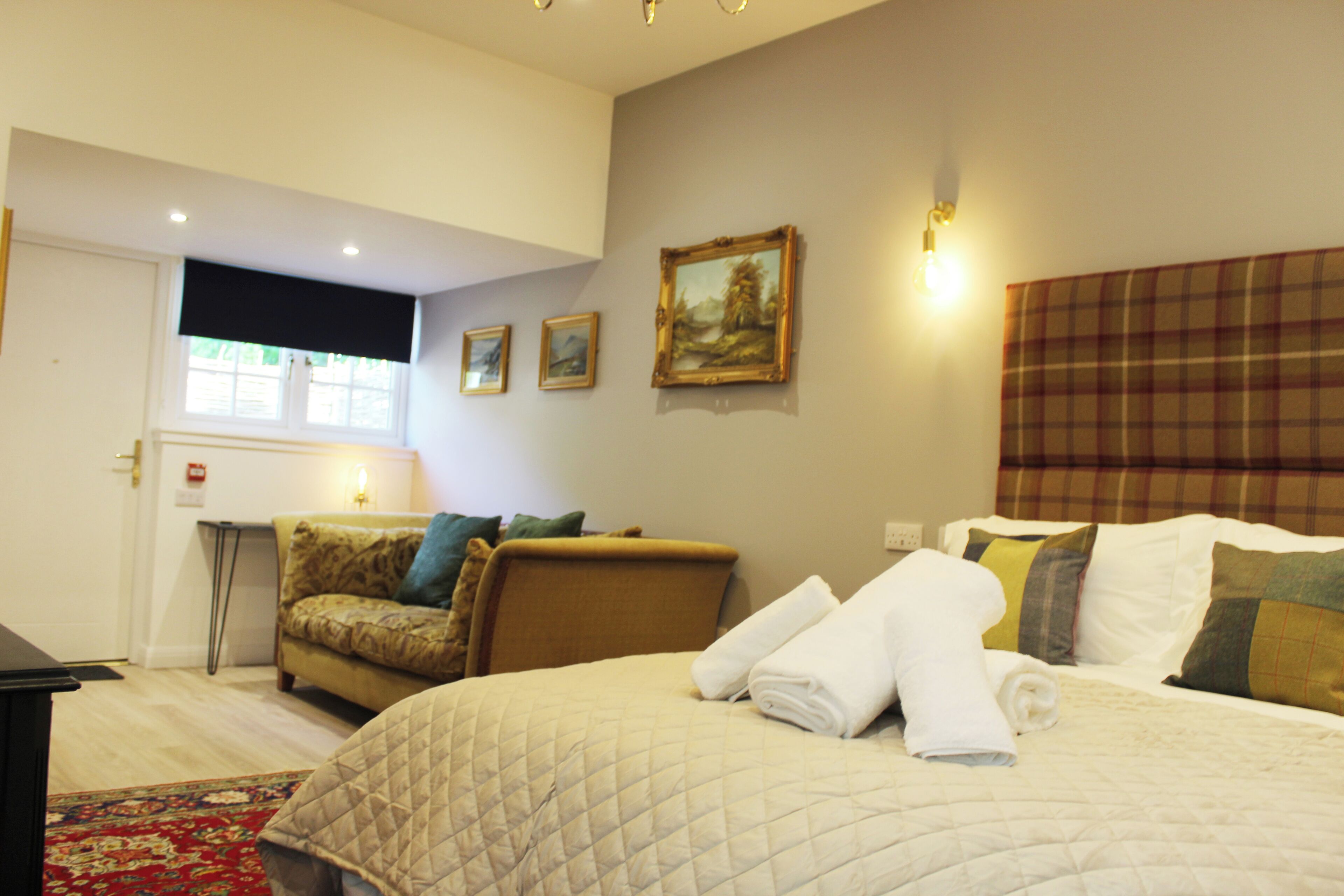 A hotel room with a bed, a sofa, a window, and a painting on the wall.