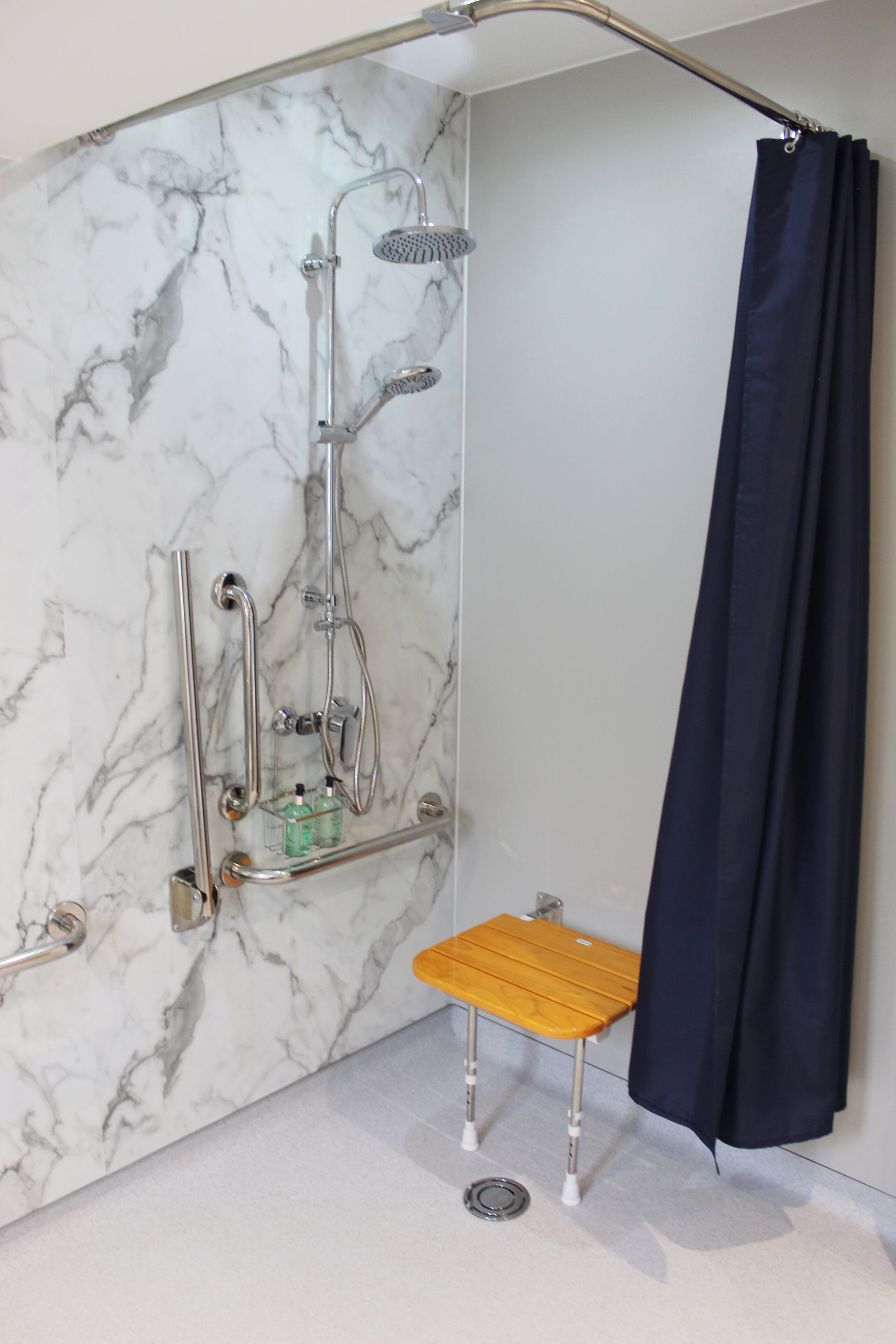 Eine moderne Dusche mit einer Marmorwand, einem hölzernen Hocker und einem dunkelgrauen Duschvorhang.