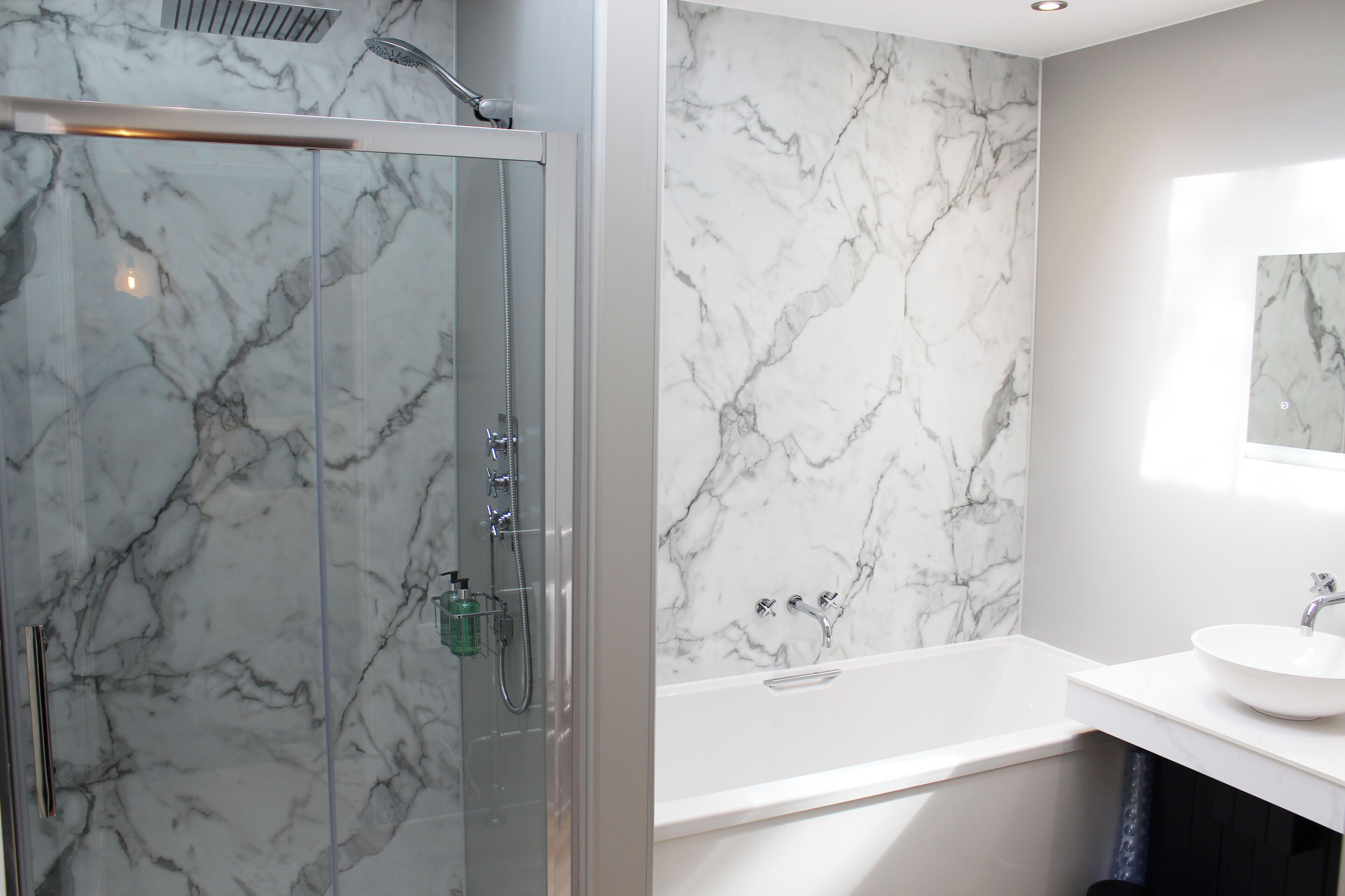 A modern bathroom with a glass-enclosed shower, a marble wall, and a white sink.