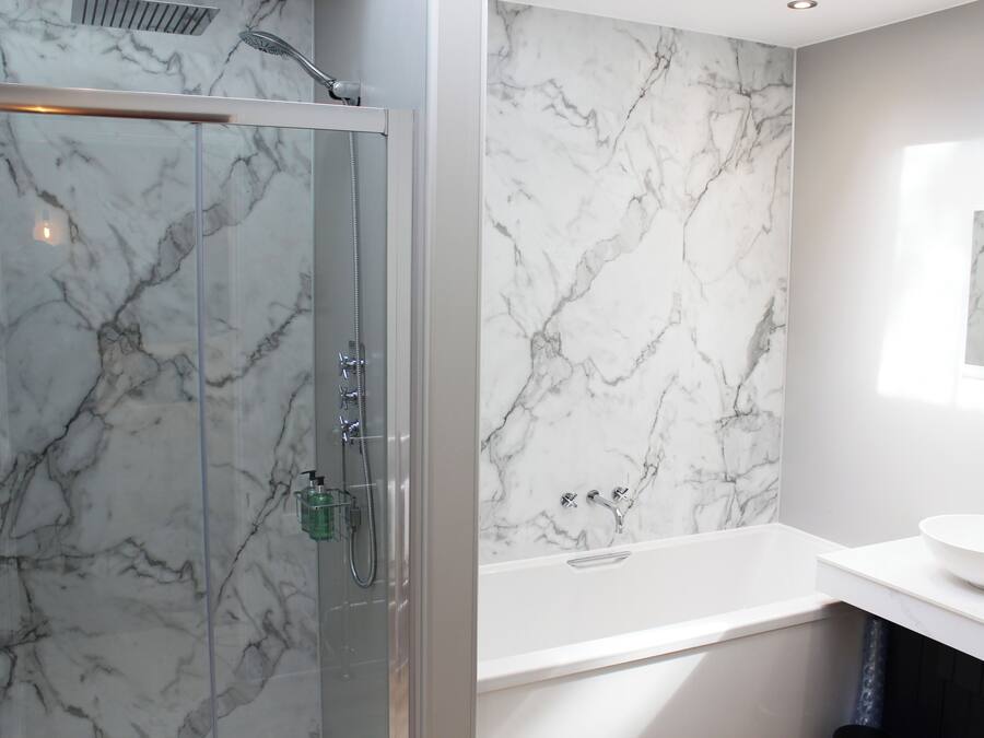 A modern bathroom with a glass-enclosed shower, a marble wall, and a white sink.