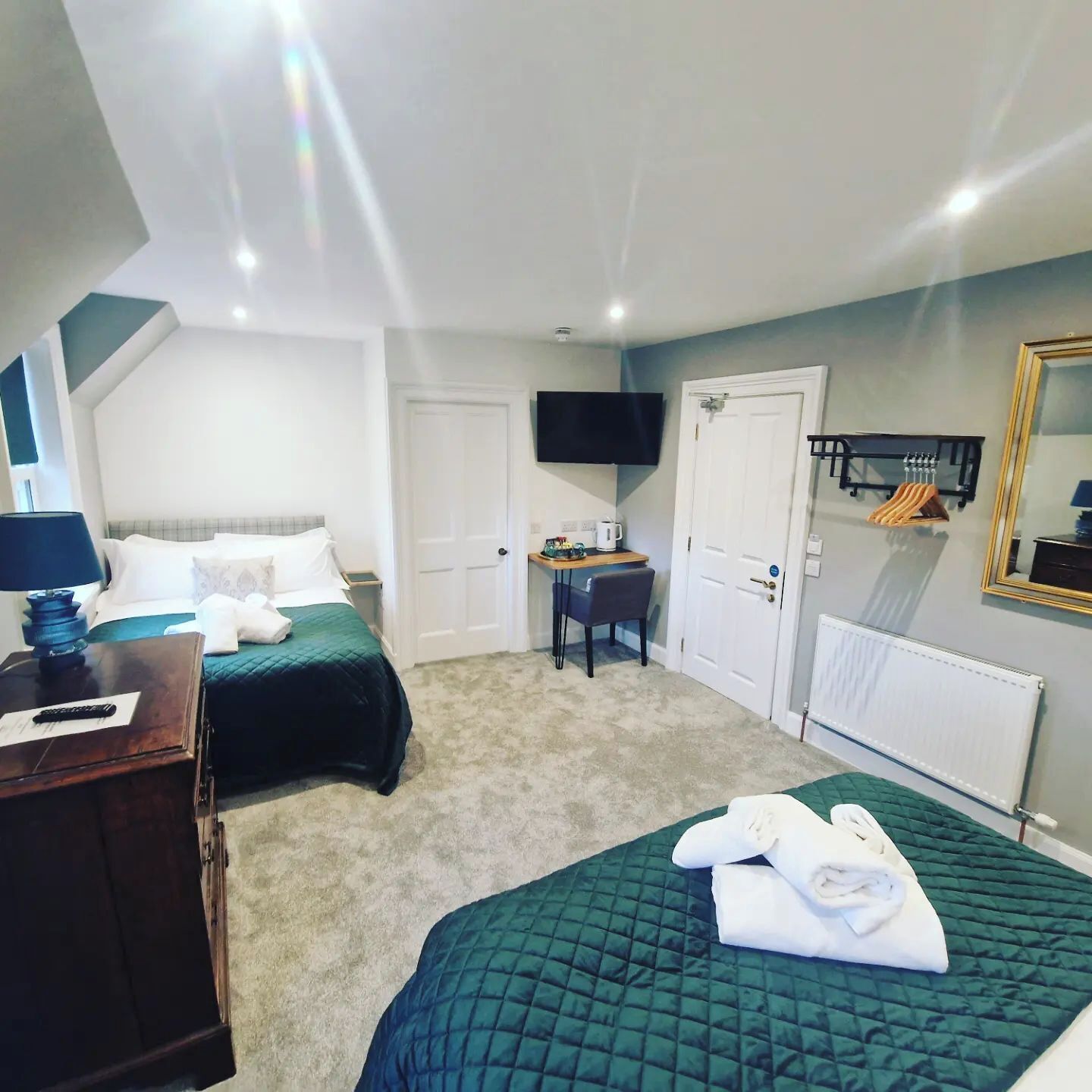 A hotel room with two beds, a desk, a television, and a mirror.