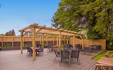 An outdoor patio with wooden tables and chairs, a pergola structure, and a wooden fence.