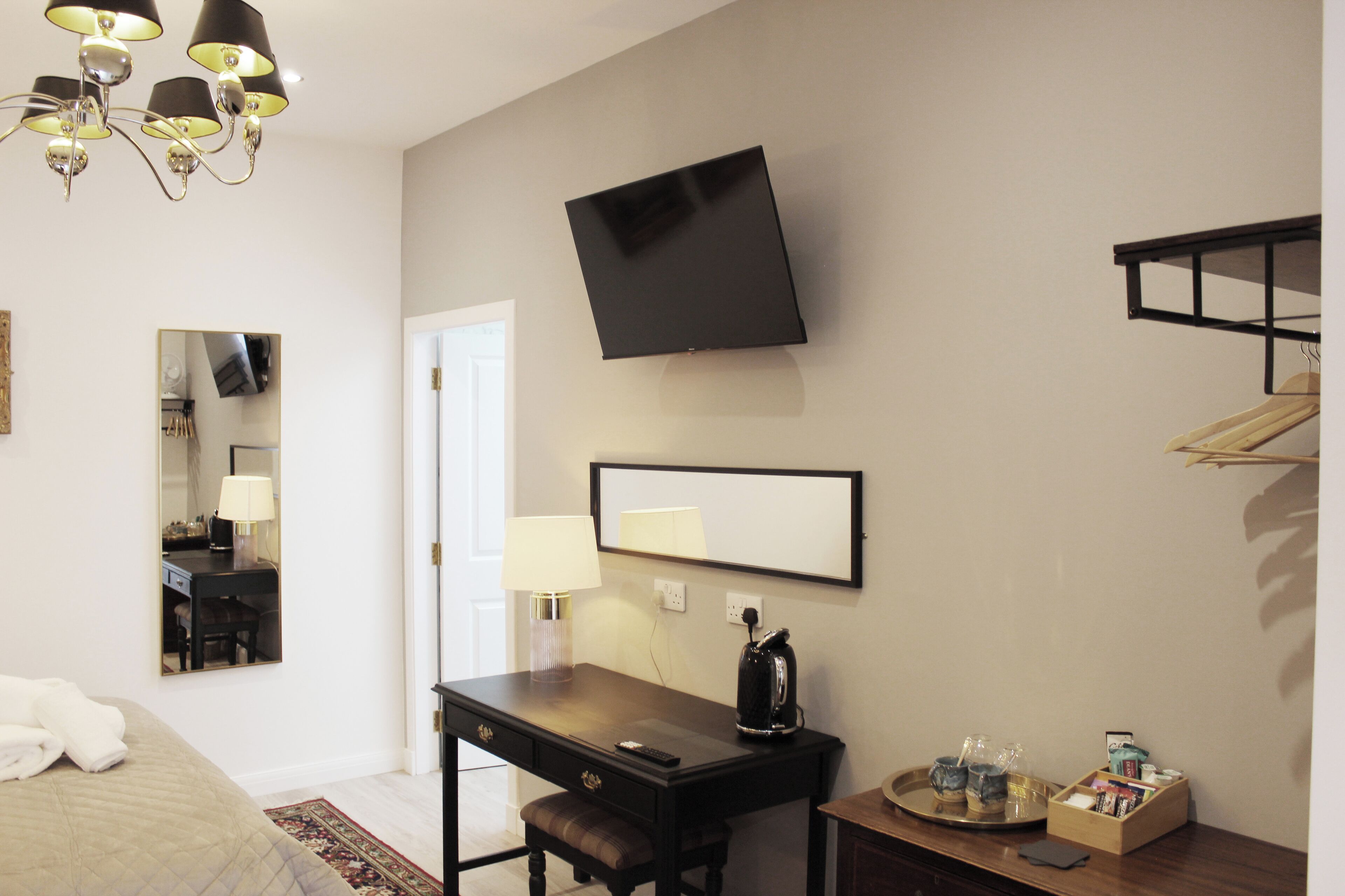 Habitación de hotel con cama, escritorio, silla, televisor de pantalla plana, lámpara de noche y una mesita con bandeja.