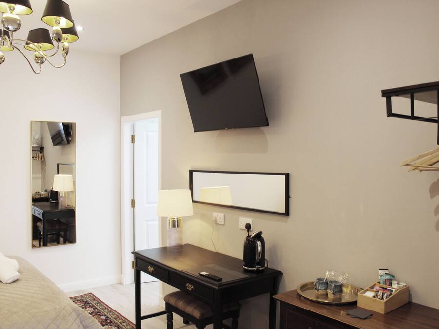 Habitación de hotel con cama, escritorio, silla, televisor de pantalla plana, lámpara de noche y una mesita con bandeja.