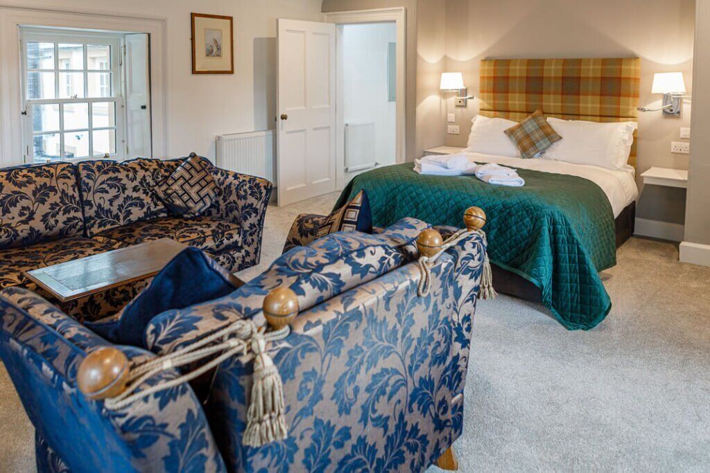 Una habitación de hotel con un sofá estampado, una cama con colcha verde y una mesita de noche con lámparas.
