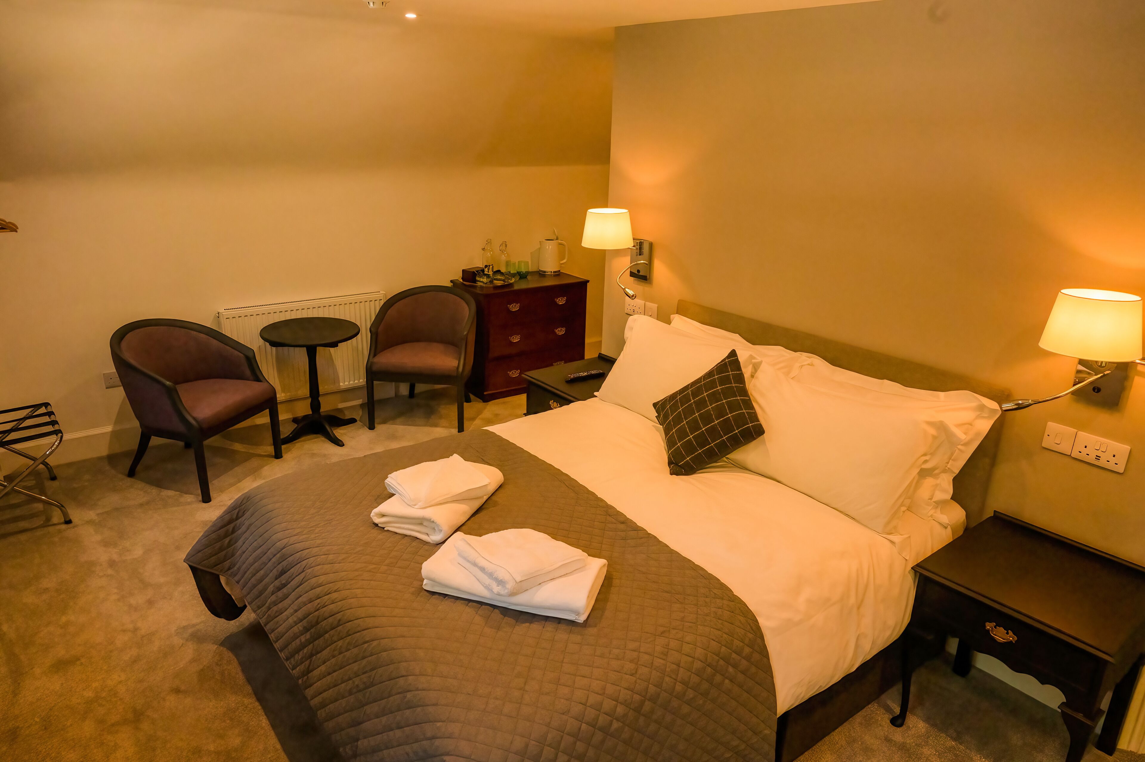 A hotel room with a bed, two chairs, a small table, a dresser, and a nightstand.