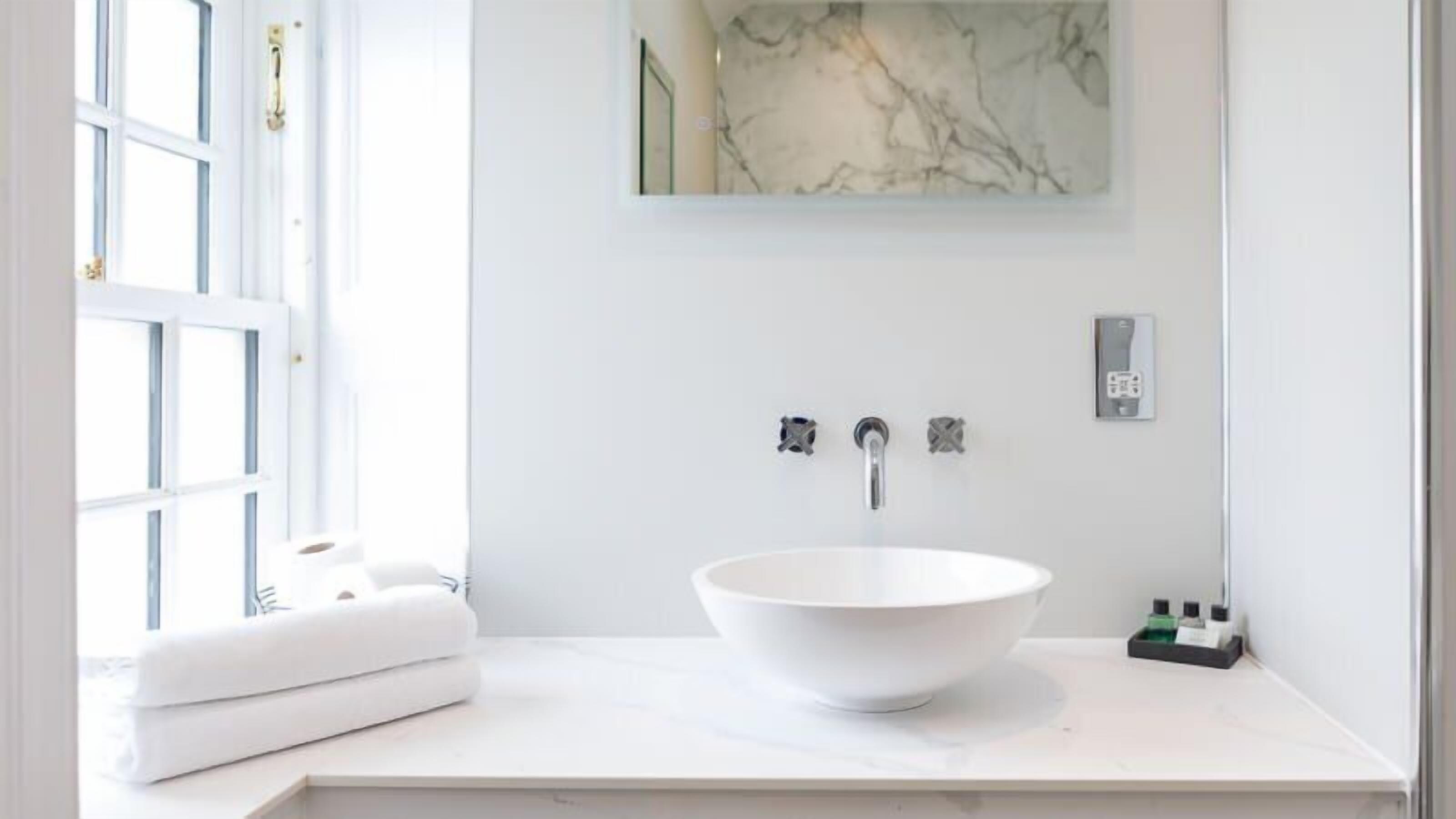 A bathroom with a white sink, a marble backsplash, and a window with white curtains.