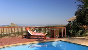Ein Poolbereich mit Liegestuhl, Blick auf die Landschaft und einem strohgedeckten Gebäude.