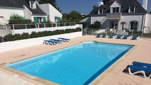 A rectangular swimming pool with blue water, surrounded by a tiled deck. There are blue lounge chairs and a white fence with a flower bed.
