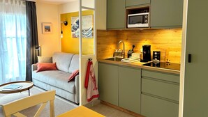 A compact living space with a kitchenette, a sofa, a dining table, and a view through a window.