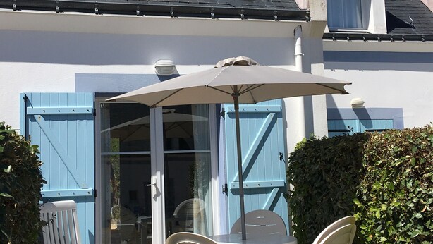 A house with a patio area featuring a table and chairs, a blue door, and a white umbrella.