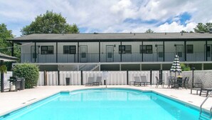 Ein zweistöckiges Hotel mit Swimmingpool, Außenbereich zum Sitzen und einem umzäunten Patio.