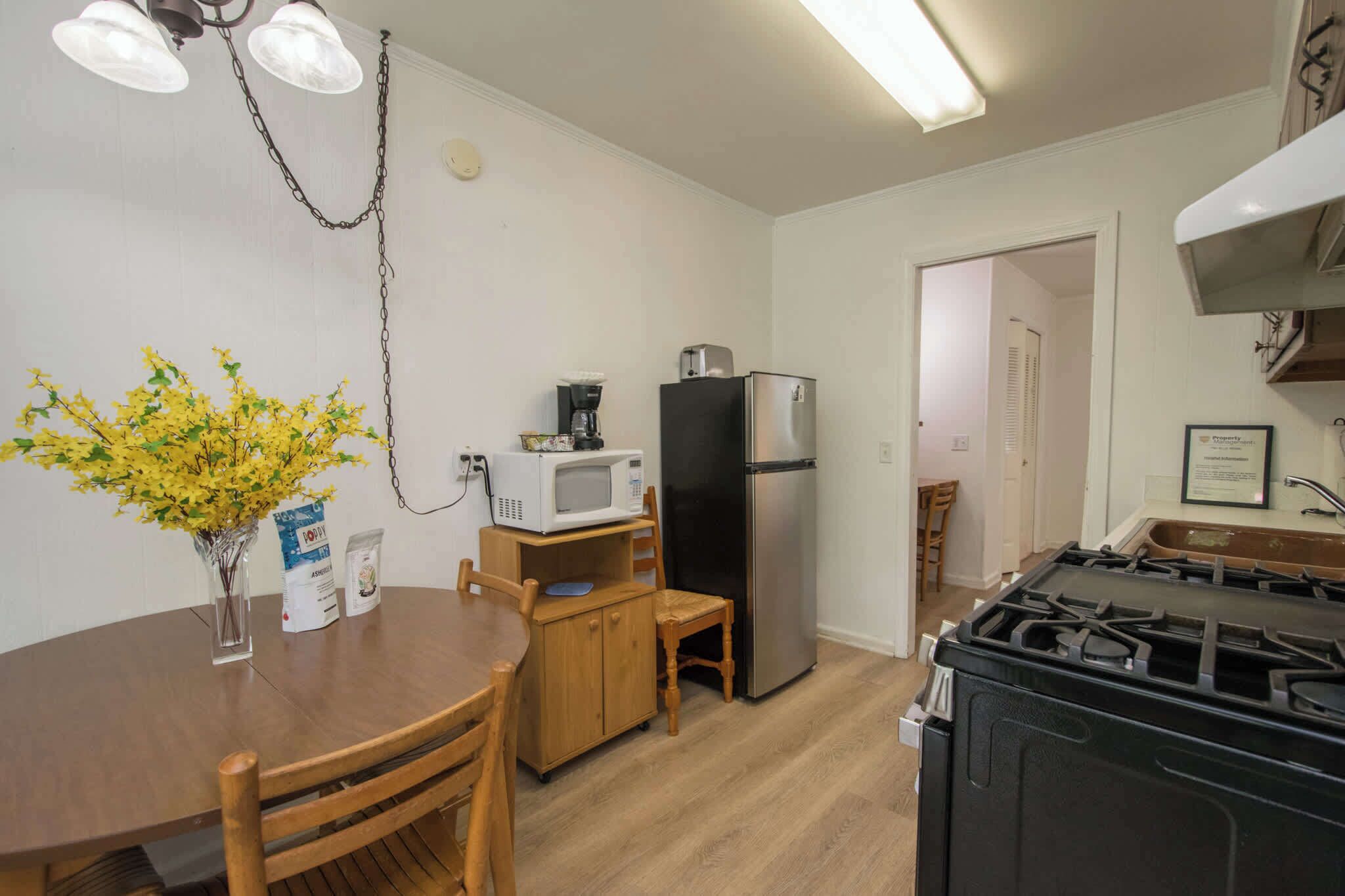 A compact kitchen with a dining table, chairs, a refrigerator, a microwave, and a gas stove.