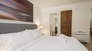 Ein Hotelzimmer mit einem großen Bett, einer Nachttischlampe, einem Holzschrank und einem durch eine offene Tür einsehbaren Badezimmer.