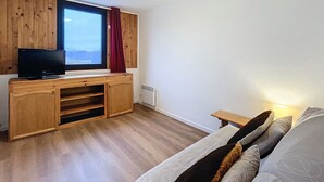 Un dormitorio con un mueble de televisión de madera, un televisor de pantalla plana, una ventana con vistas, una cama con almohadas y una mesita de noche.
