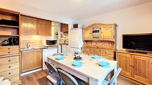 Cocina compacta con armarios de madera, microondas, lavavajillas y una mesa de comedor para cuatro personas, con platos azules.